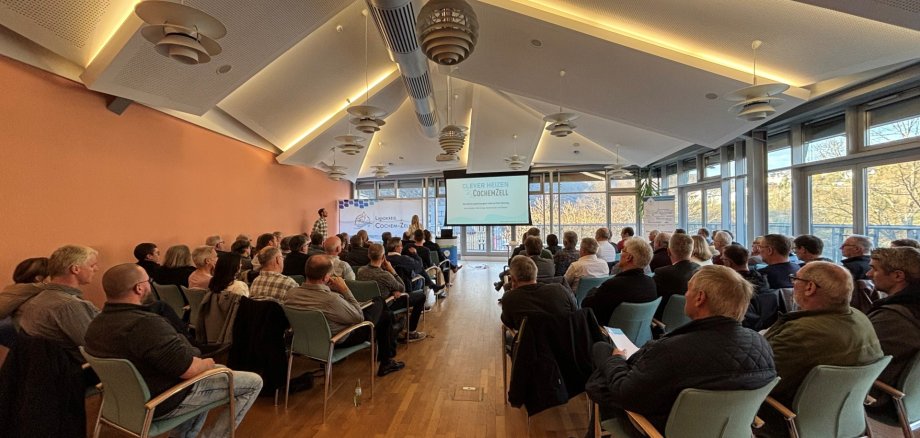 Viele Besucherinnen und Besucher sitzen in einem großen Saal und hören der Landrätin zu.