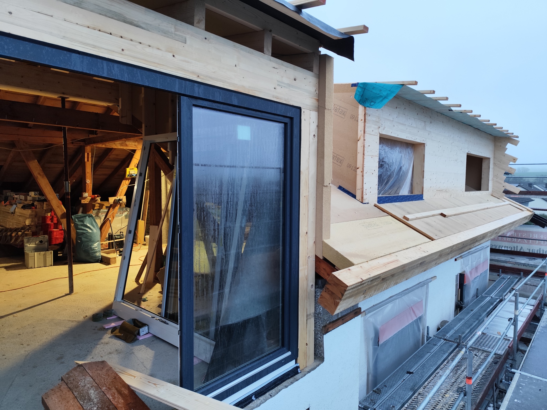 Foto eines Sanierungsvorhabens; neues Dach mit neu eingebauten Fenster im Hintergrund der Dachstuhl mit weiteren Baumaterialien zu sehen