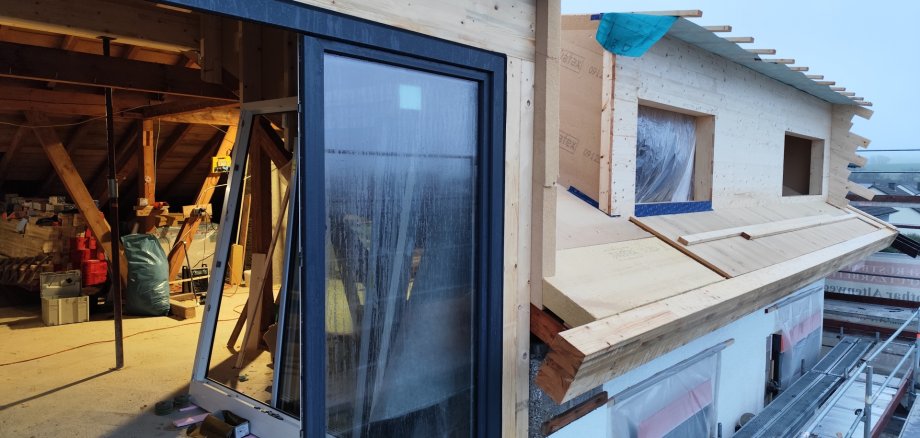 Sanierungsvorhaben "Clever heizen - einfach sanieren" Foto eines Sanierungsvorhabens; neues Dach mit neu eingebauten Fenster im Hintergrund der Dachstuhl mit weiteren Baumaterialien zu sehen