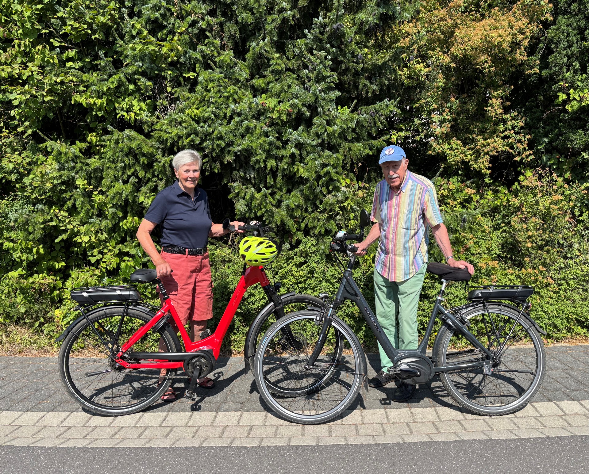Das Ehepaar von Stackelberg (beide 85) mit ihren Fahrrädern vor einer grünen Hecke.