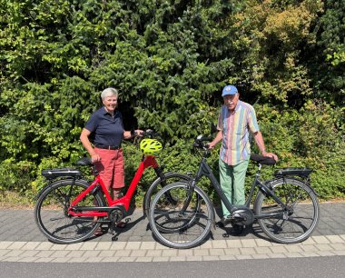 Das Ehepaar von Stackelberg (beide 85) mit ihren Fahrrädern vor einer grünen Hecke.