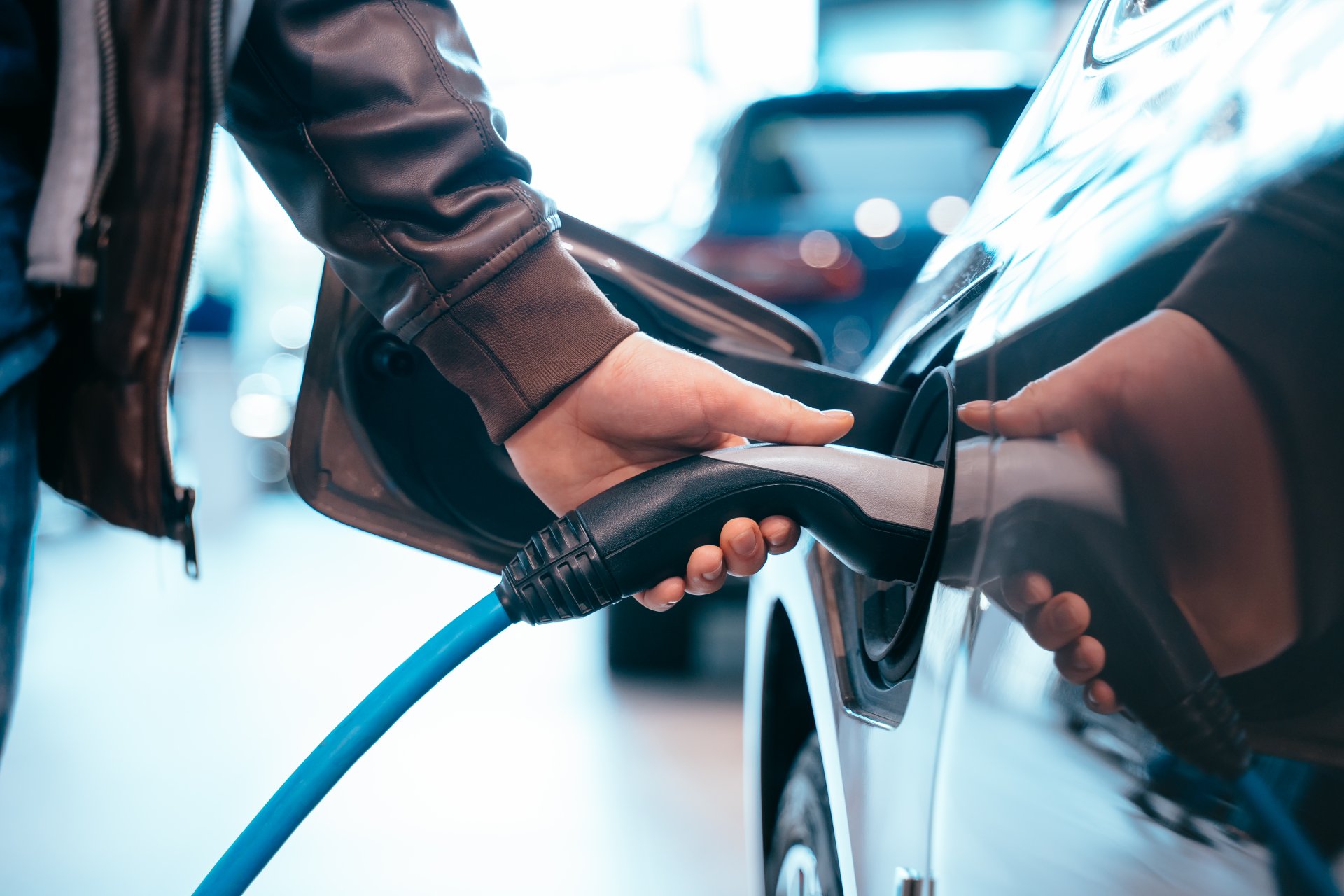Eine menschliche Hand hält den Ladestecker eines Elektroautos und verbindet ihn mit dem Fahrzeug.