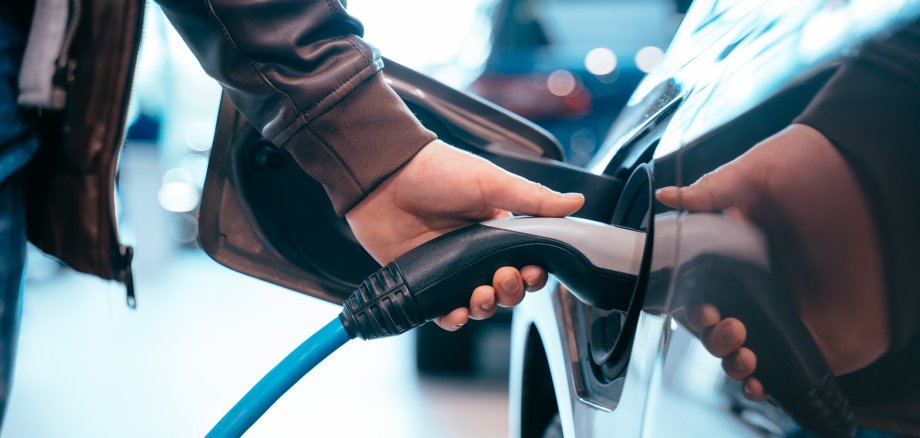 E-Auto Eine menschliche Hand hält den Ladestecker eines Elektroautos und verbindet ihn mit dem Fahrzeug.
