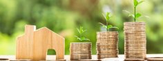 Abbildung von Haus neben drei Stapeln von Geldmünzen, auf denen jeweils Pflanzen wachsen